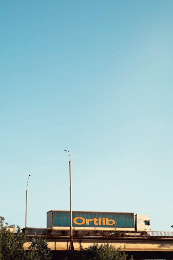 A large truck crosses a bridge under a clear blue sky, suggesting transportation or logistics.